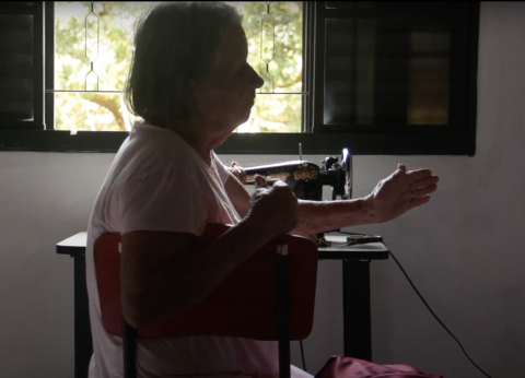 mulher está sentado, ao lado de uma máquina de costura.#paratodosverem