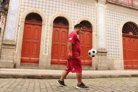 homem passa em frente à antigo casarão - a casa da frontaria azulejada - ele caminha e a bola está no ar. #paratodosverem