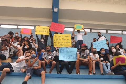 crianças mostram cartazes sentadas na arquibancada #paratodosverem