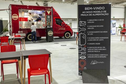 painel ao lado de mesa e cadeira com orientações sanitárias. #paratodosverem