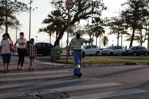 agente da CET estende o braço sobre faixa de segurança. Ao fundo estão os pedestres que começam a atravessar. #paratodosverem