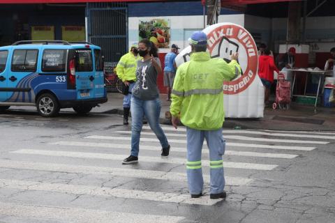 Mulher atravessa a rua e agente faz gesto do braço estendido. #paratodosverem