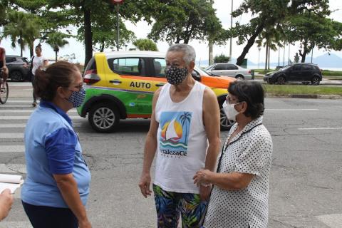 Casal de idosos conversa com agente da CET próximo a uma faixa de pedestres. #paratodosverem