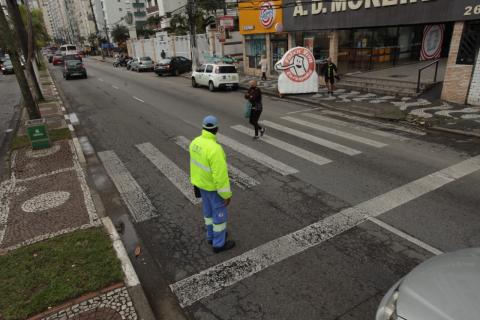 agente da CET em primeiro plano sobre a faixa. Uma pessoa atravessa a avenida. Ao fundo, o inflável da campanha. #paratodosverem
