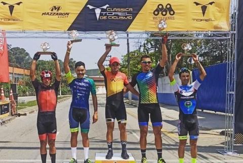 Cinco ciclistas erguendo seus troféus #paratodosverem