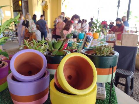 vasos vazios e vasos com plantas em primeiro plano. São objetos expostos em feira. Ao fundo se vê movimentação de pessoas em outras bancas de feirinha. #paratodosverem