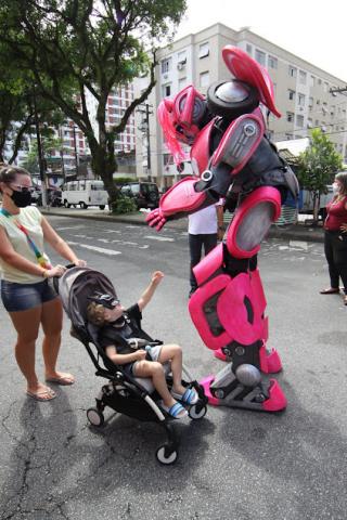 mãe empurra carrinho e criança estende a mão para o megatron. #paratodosverem