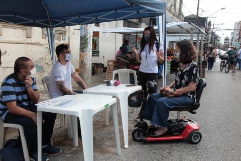 Estande do setor de atendimento a pessoas com deficiência. Uma cadeirante está à frente. #paratodosverem