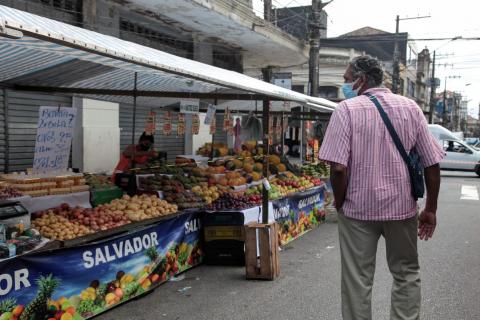 Barracas e legumes e frutas. Homem passa diante de barracas. #paratodosverem