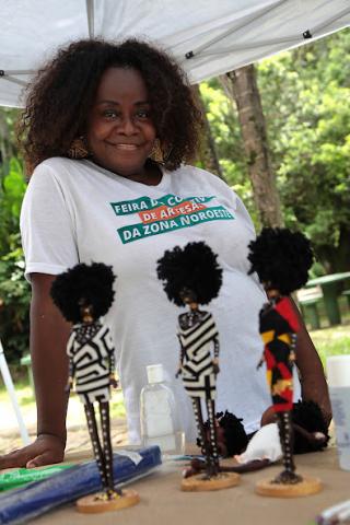 Mulher negra com cabelo afro e bonecas com cabelo afro na sua frente. #pratodosverem