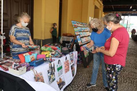 Mulheres observam produtos artesanais em feira no Valongo. #pracegover