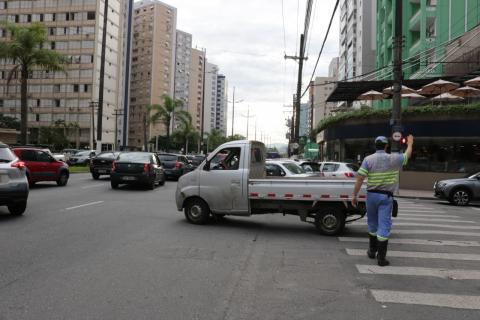 Agente da CET está em cruzamento de rua e avenida sinalizando para veículos. Ele está caminhando sobre a faixa de pedestres. #Paratodosverem