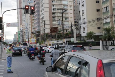 Motorista está próximo a canteiro central, em frente a um semáforo. Ele sinalizada para os veículos. #Paratodosverem