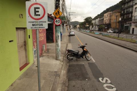Em primeiro plano, uma placa de permitido estacionar para motos em rua de Santos. #paratodosverem