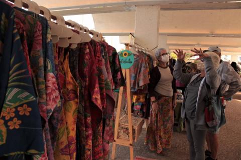 #pracegover mulher observa roupas penduradas para comércio