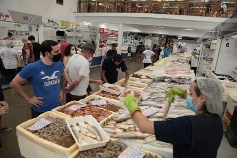 pessoas olhando frutos do mar e peixes em barraca #paratodosverem