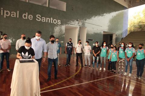Atleta assina contrato com pessoas olhando ao fundo. #paratodosverem