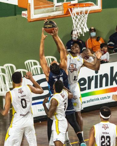jogador de santos vai arremessar na cesta e está cercado por três jogadores da equipe adversária. #paratodosverem