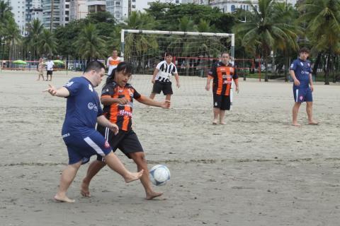 lance de jogo com dois jovens dividindo a bola. A trave está ao fundo com jogadores de defesa na frente. #paratodosverem