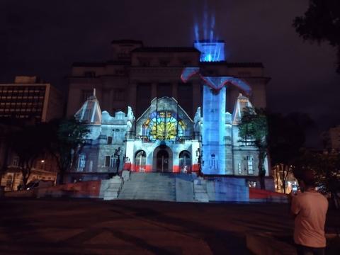 fachada comprojetção de castelo. Na praça, à direita, uma pessoa olha para a imagem. #paratodosverem