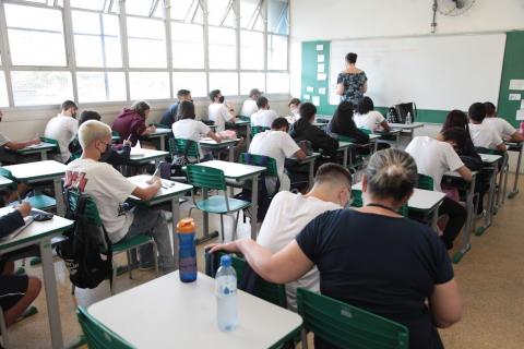 Giovanni está sentado com a auxiliar de classe ao lado dele. #paratodosverem