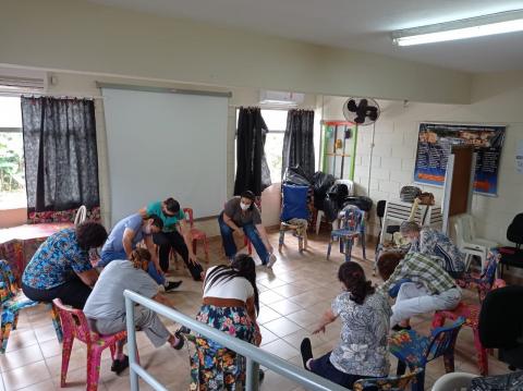 Pessoas dentro de uma sala, em circulo, se exercitando. #paratodosverem