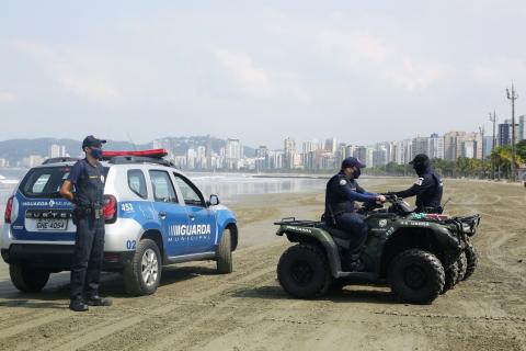 Viatura da guarda municipal na faixa de areia, um guarda em pé e outros dois em quadriciclos. #Paratodosverem