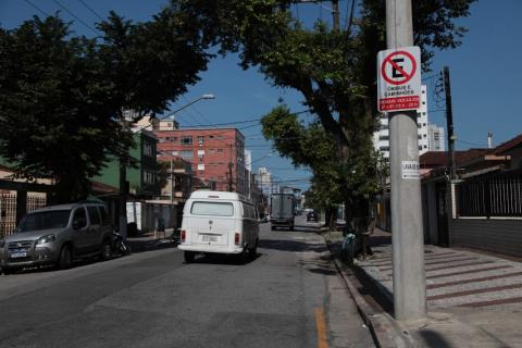 carro passa pela rua. Posto do lado direito tem placa que orienta sobre proibição de estacionamento. #paratodosverem