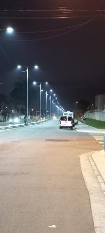 vista geral da via com as luminárias de vários postes acesas. #paratodosverem
