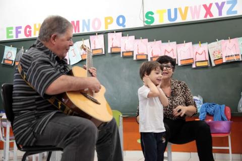 Idoso toca violão em atividade com criança em escola. #paratodosverem