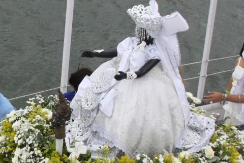 imagem da santa envolvida em flores está dentro de embarcação para cortejo marítimo. #paratodsverem