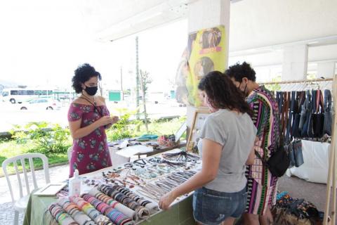 duas mulheres olham produtos em barraca #paratodosverem