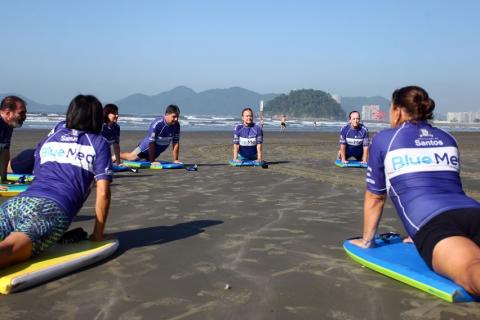 em circulo na areia, pessoas treinam manobras de surfe. #paratodosverem