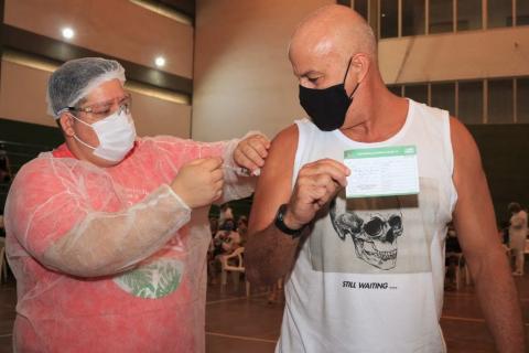 Homem com máscara facial recebe injeção de vacina no interior de ginásio