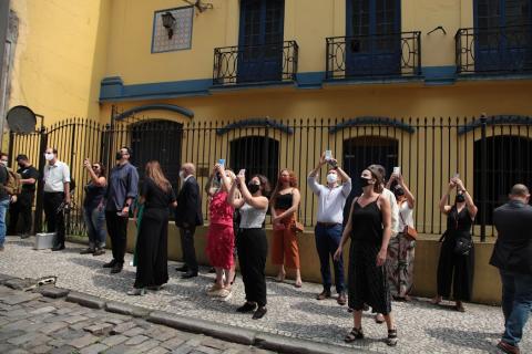 Pessoas na calçada filmam apresentam de músicos #paratodosverem