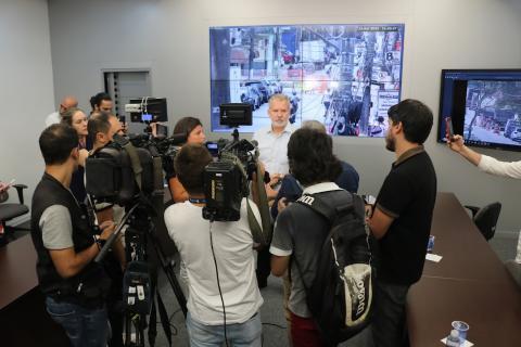 secretario estadual cercado por jornalistas com telão ao fundo #paratodosverem