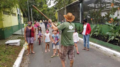 guia aponta para árvore enquanto crianças e adultos observam. #paratodosverem