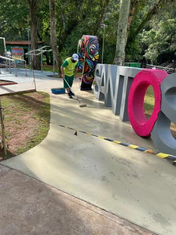 homem está varrendo o chão ao lado do monumento Amo Santos. #paratodosverem