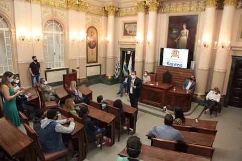 sala princesa isabel com pessoas sentadas no plenário e outras na mesa principal. Uma delas está em pé falando ao público. #paratodosverem