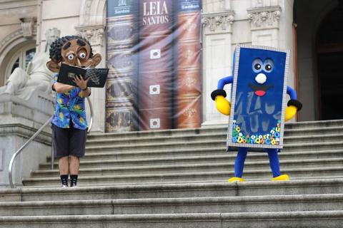 bonecos que remetem à leitura na escadaria da praça municipal. Um painel que imita três livros em estante estampa a entrada da prefeitura. #paratodosverem