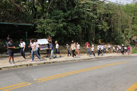 Crianças na calçada enfileiradas levando casinha #paratodosverem