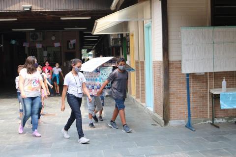 Crianças saindo da escola carregando casinha #paratodosverem