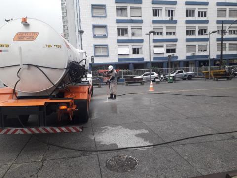 caminhão pipa à esquerda e homem ao fundo esguichando água no piso. #paratodosverem