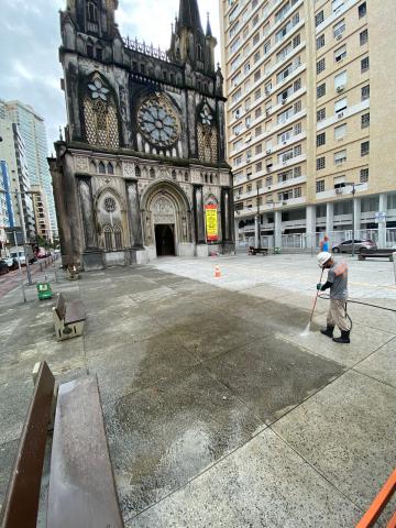 homem esguicha água no piso com a basílica ao fundo. #paratodosverem