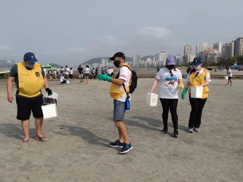 pessoas caminham pela areia carregando caixas para depósito de lixo. #paratodosverem