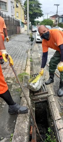 homens seguram saco de lixo ao lado de boca de lobo. #paratodosverem