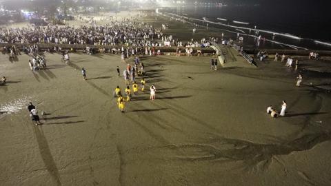 vista geral e aérea da faixa de areia, com uma equipe de limpeza e algumas pessoas vestidas de branco espalhadas. #paratodosverem