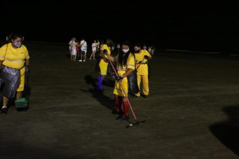 mulheres uniformizadas varrem faixa de areia. Elas seguram vassouras e sacos plásticos #paratodosverem