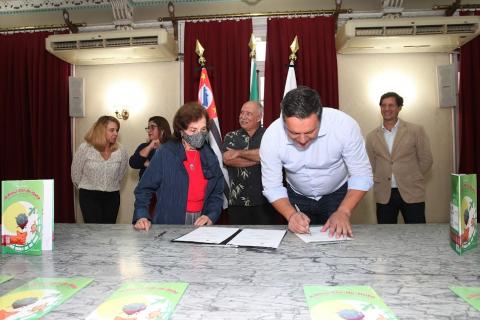 prefeito assina livro sobre uma mesa. #paratodosverem