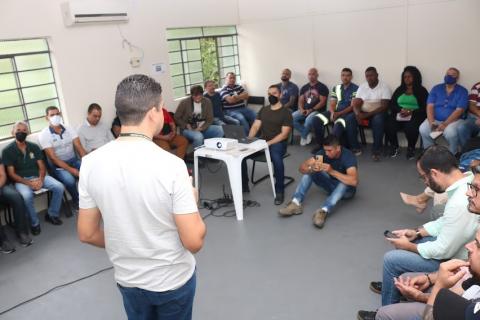 reunião de pessoas em sala, com uma delas em pé falando a todos. #paratodosverem